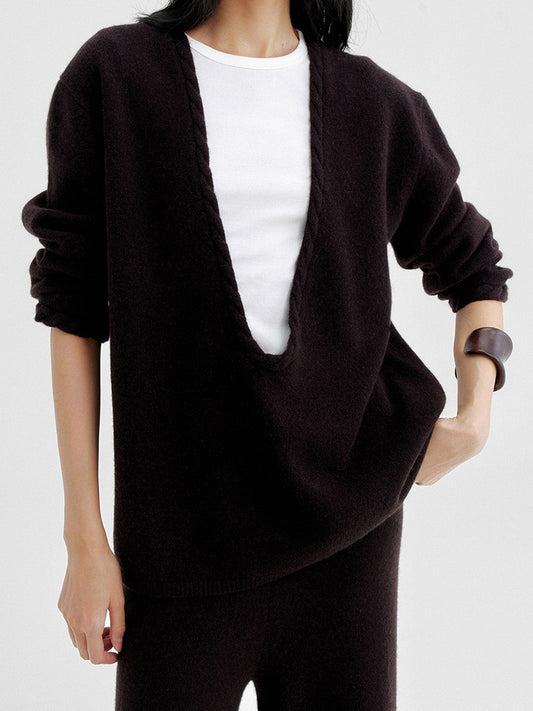 Woman wearing Arkin Studio cable knit v-neck wool sweater in dark-brown with a white top inside, matching knit pants, standing facing the camera, on a white background