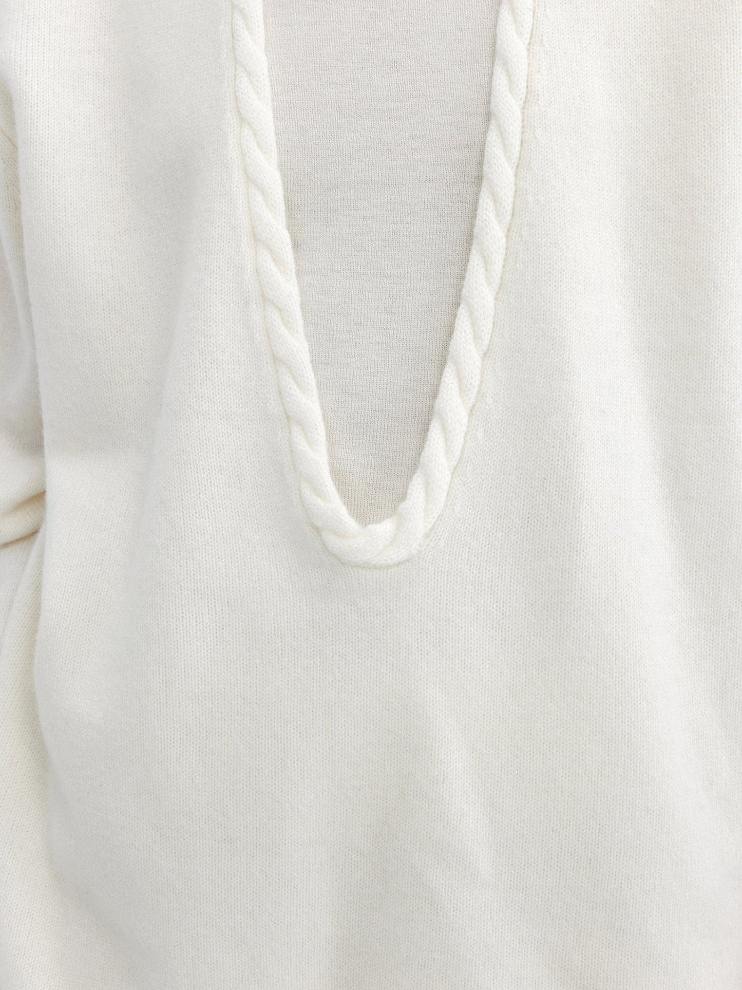 Close up of a woman wearing Arkin Studio cable knit v-neck wool sweater in white with a white top inside, focus on her chest, standing facing the camera, on a white background