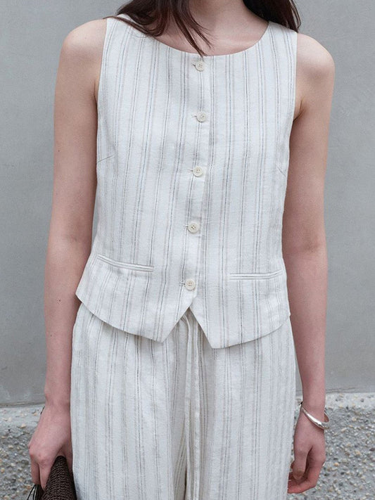 Woman wearing Arkin Studio classic striped vest in ivory and striped trousers in ivory, standing facing the camera, a wall behind her