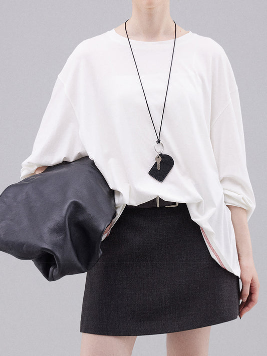 Woman wearing Arkin Studio deconstructed modal cotton long sleeve tee in white and a black skirt, holding a black handbag, standing facing the camera, on a white background