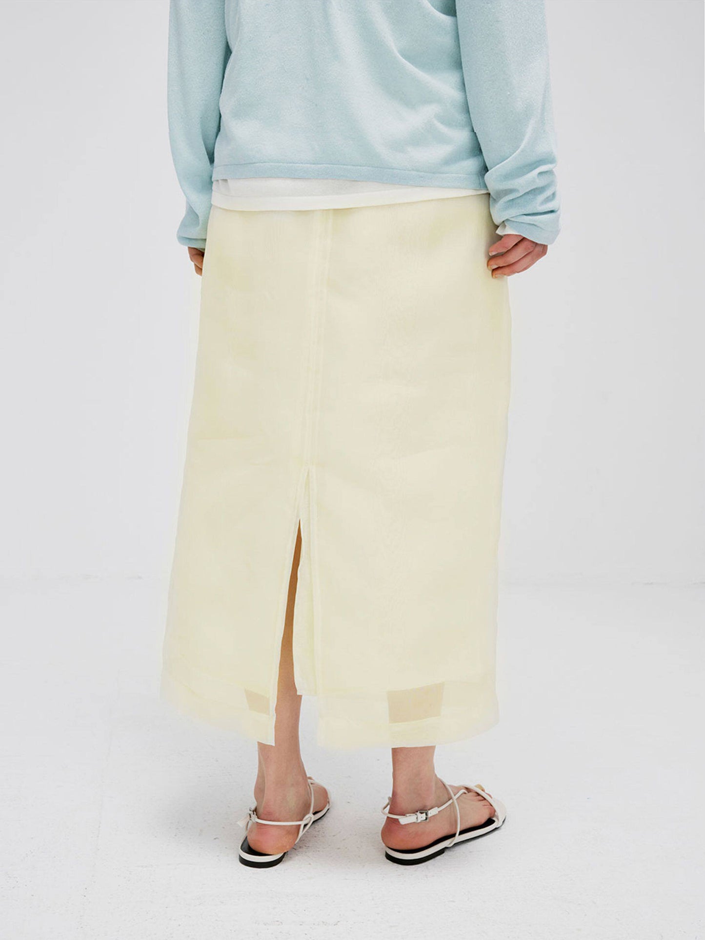 Woman wearing Arkin Studio high-waist mesh two-layer midi skirt in light yellow and a light blue long sleeve, back view, on white background