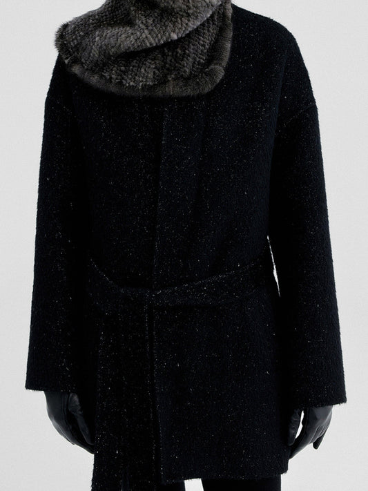 Woman wearing Arkin Studio metallic trim belted wool coat in black with furry scarf, hands down at her sides, standing facing the camera, on a white background