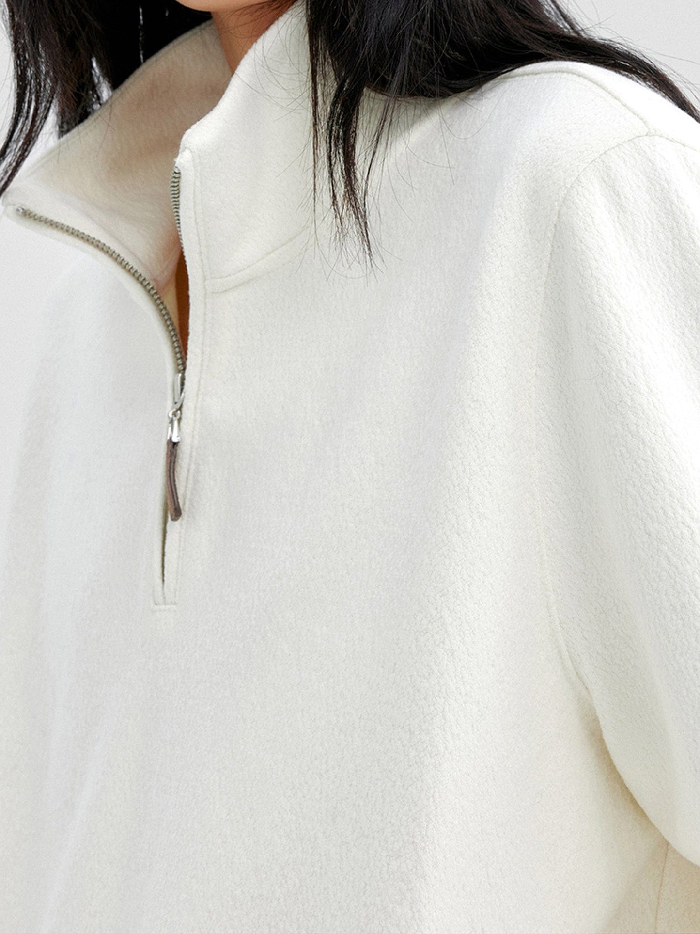 Close up of a woman wearing Arkin Studio minimalist half zip sweatshirt in ivory, focus on her chest, standing sideways, on a white background
