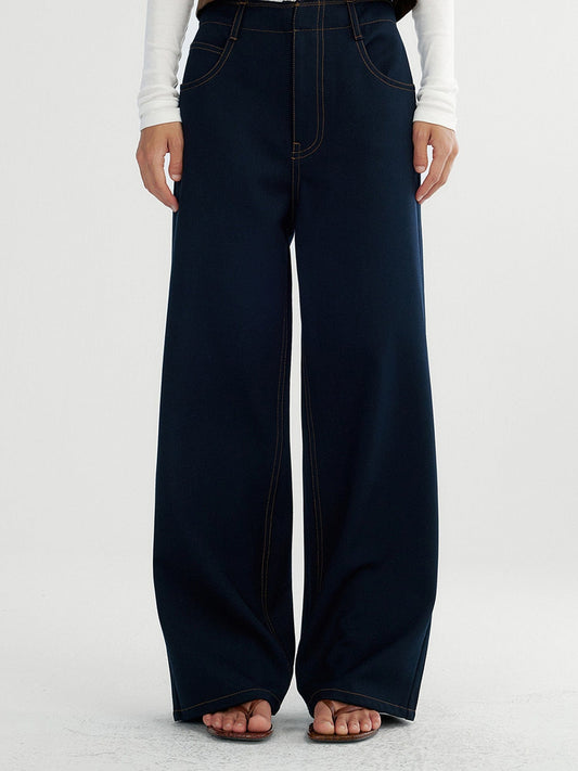 Woman wearing Arkin Studio raw edge contrast stitch trousers in dark navy, with hands down at her sides, standing facing the camera, on a white background