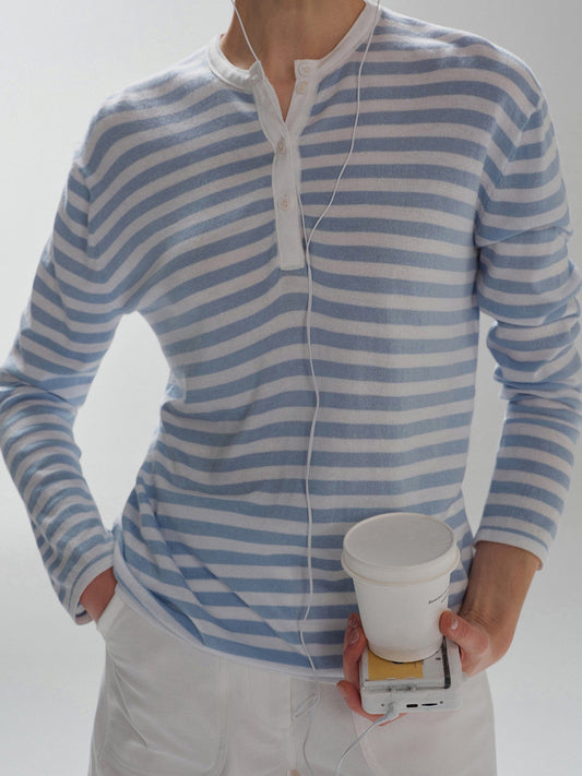 Woman wearing Arkin Studio Striped Henley Long Sleeve Tee in Light Blue, with a paper cup in her hand, standing facing the camera, on a white background