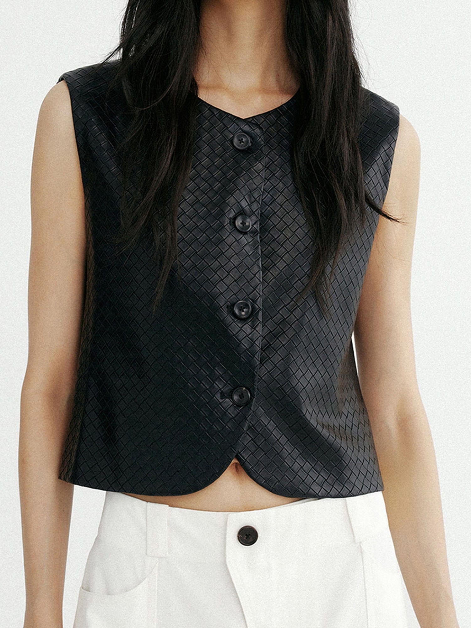 Woman wearing Arkin Studio artisan woven leather vest in black and white pants, hands down at her sides, standing facing the camera on a white background