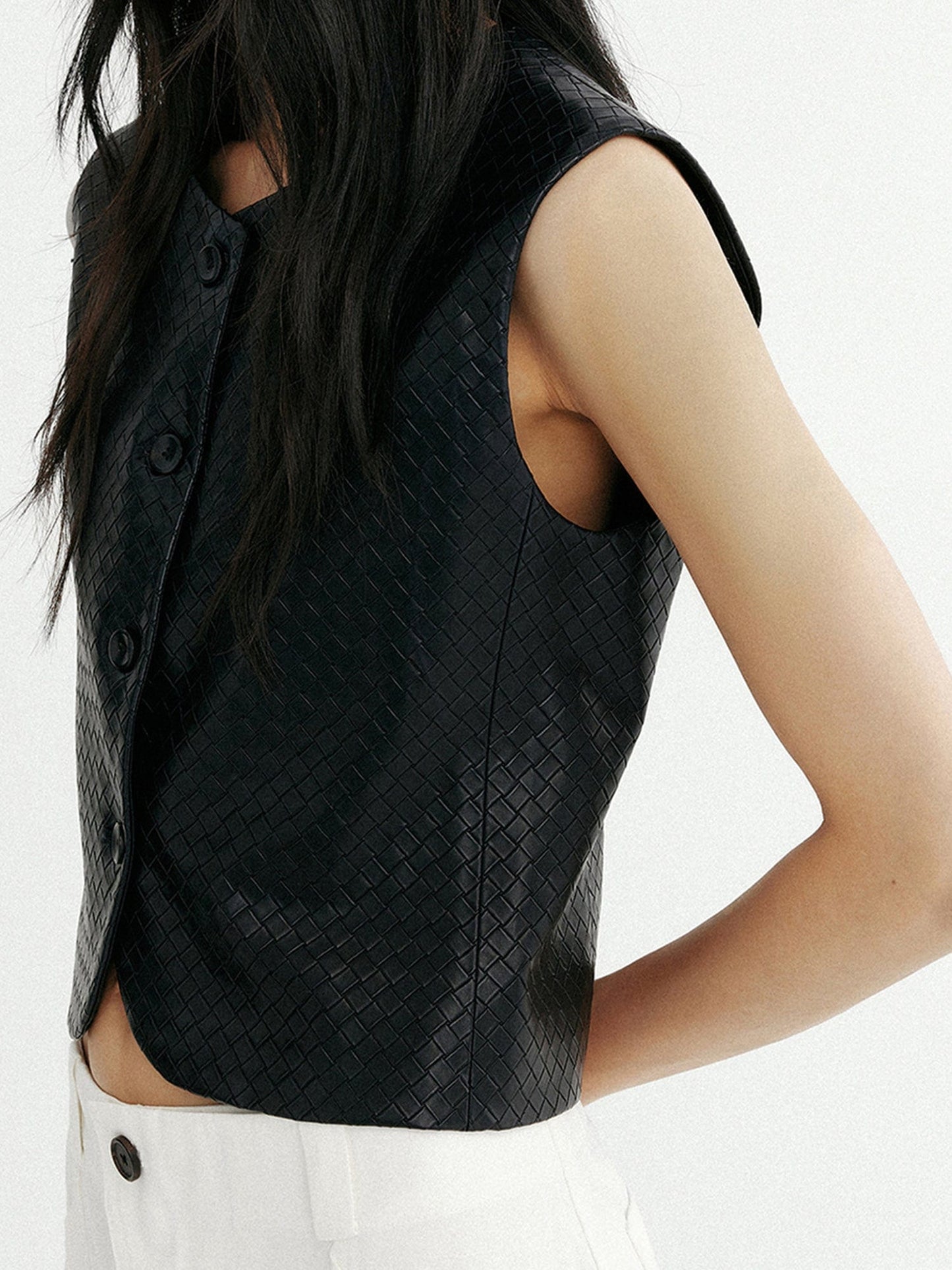 Woman wearing Arkin Studio artisan woven leather vest in black and white pants, hands behind her back, standing sideways, on a white background