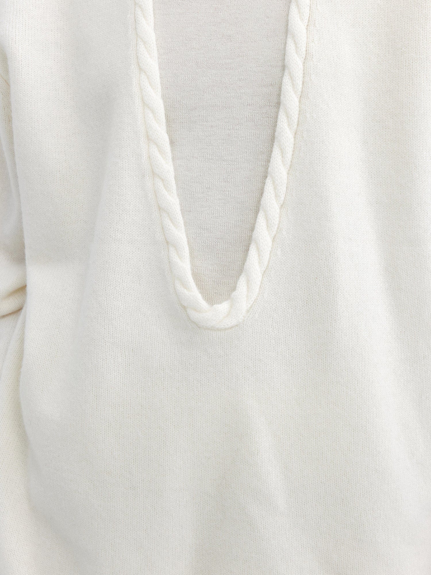 Close up of a woman wearing Arkin Studio cable knit v-neck wool sweater in white with a white top inside, focus on her chest, standing facing the camera, on a white background
