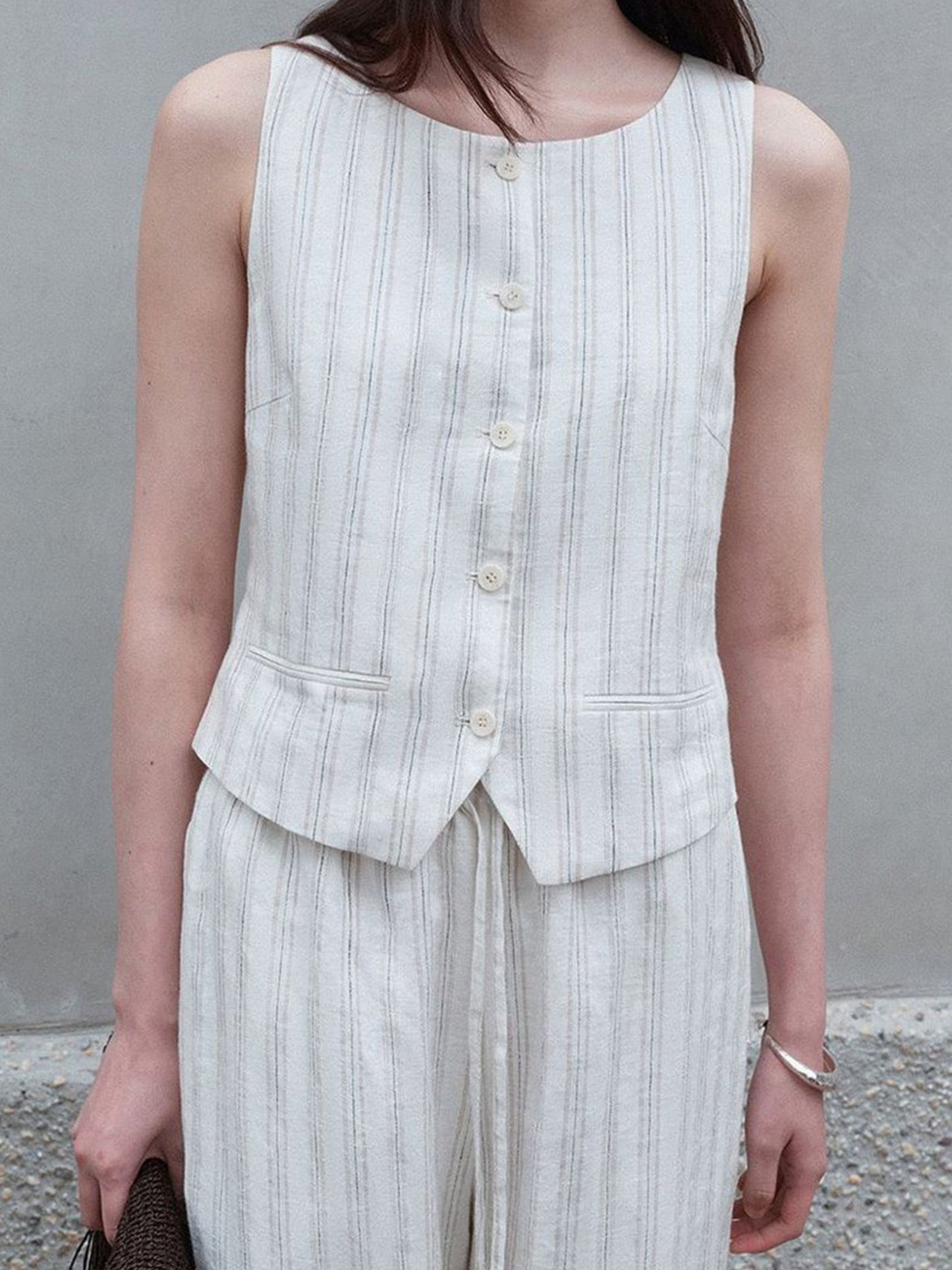 Woman wearing Arkin Studio classic striped vest in ivory and striped trousers in ivory, standing facing the camera, a wall behind her