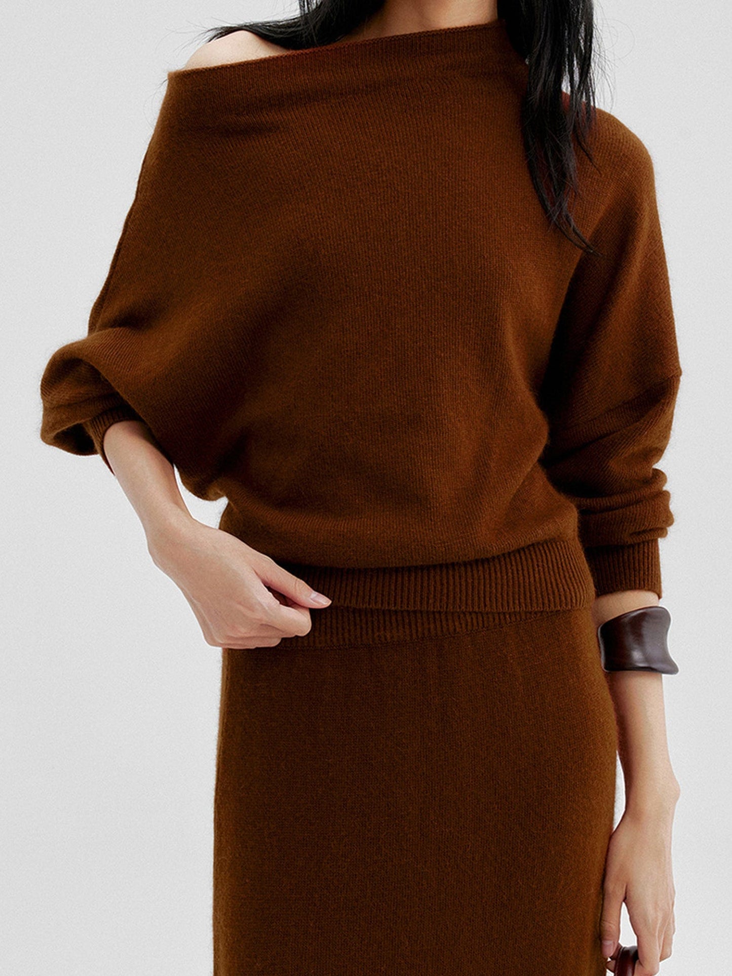 Woman wearing Arkin Studio cold shoulder slim knit top in brown and matching skirt, one hand touching the waist, standing facing the camera, on a white background