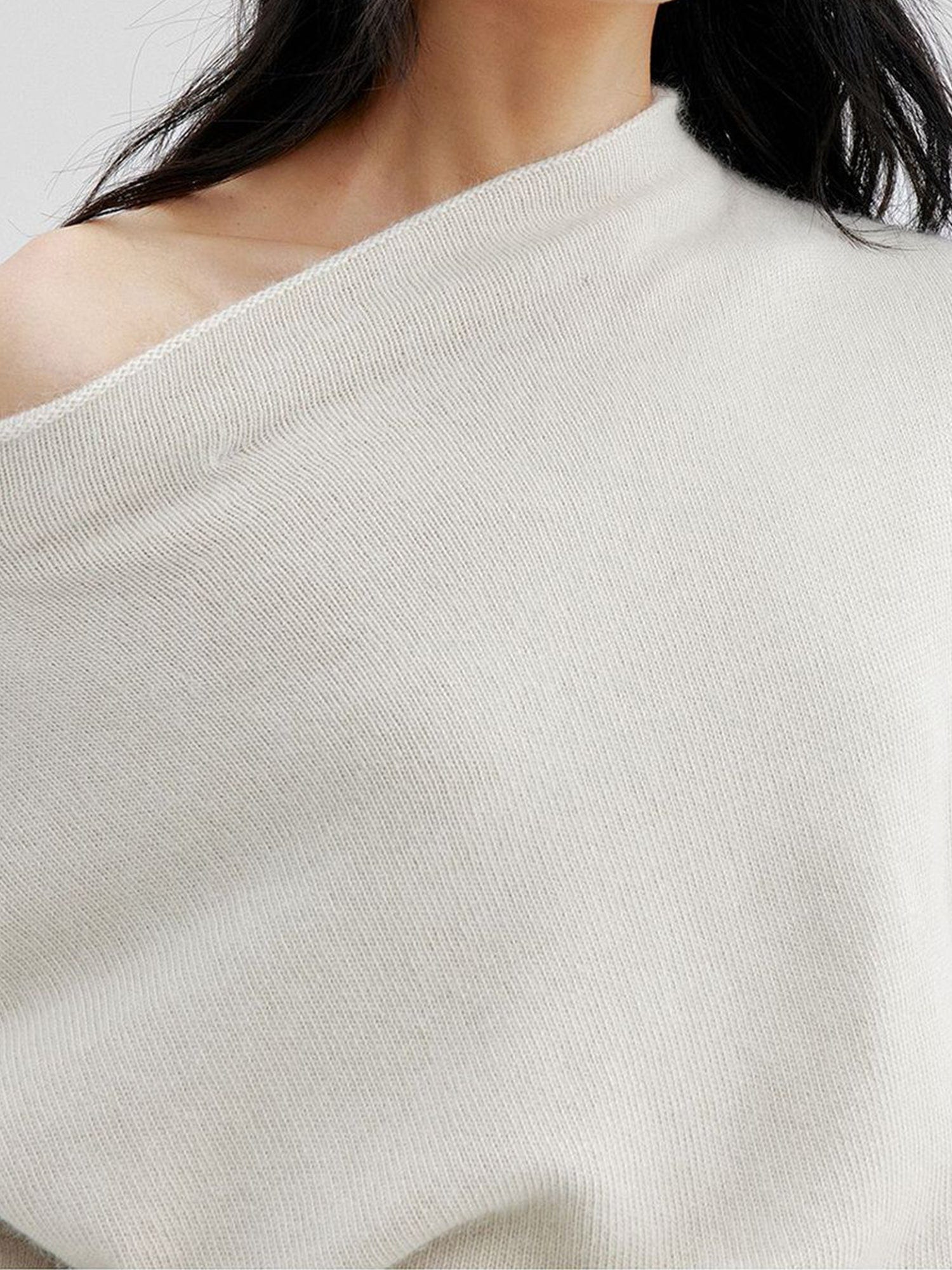 Close-up of a woman's right shoulder wearing Arkin Studio cold shoulder slim knit top in ivory, with the off-shoulder neckline pulled down to reveal part of the right shoulder, standing facing the camera, on a white background
