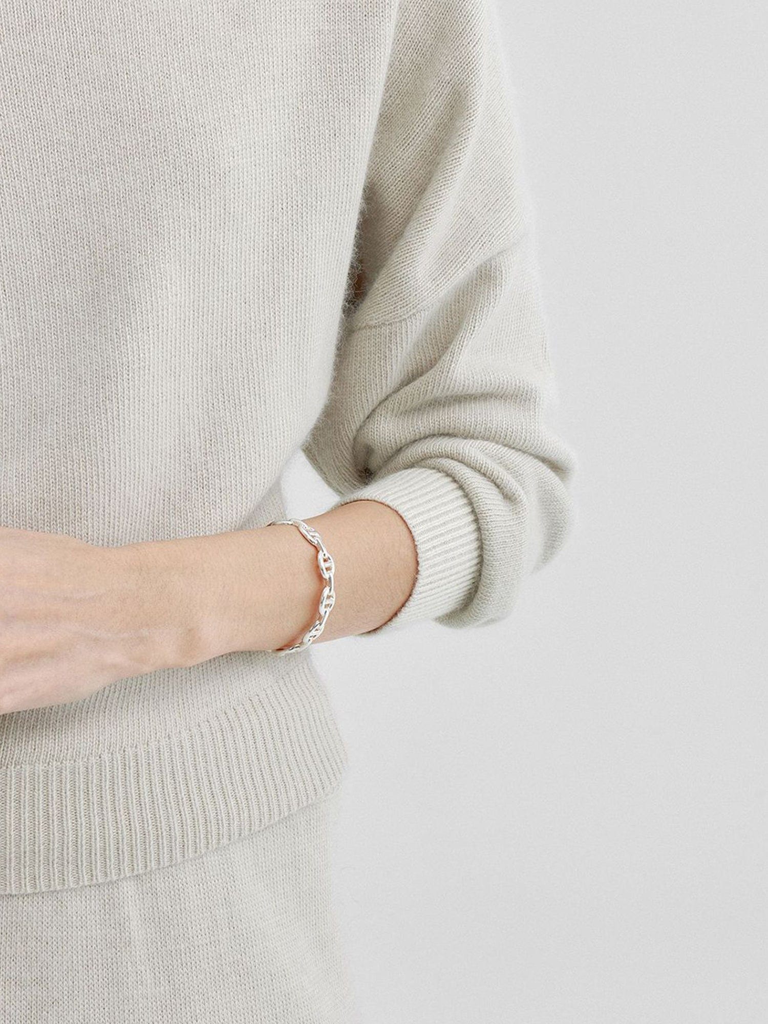 Close-up of a woman wearing Arkin Studio cold shoulder slim knit top in ivory, focus on her left arm with a silver jewelry and upper part of her left body, standing facing the camera, on a white background