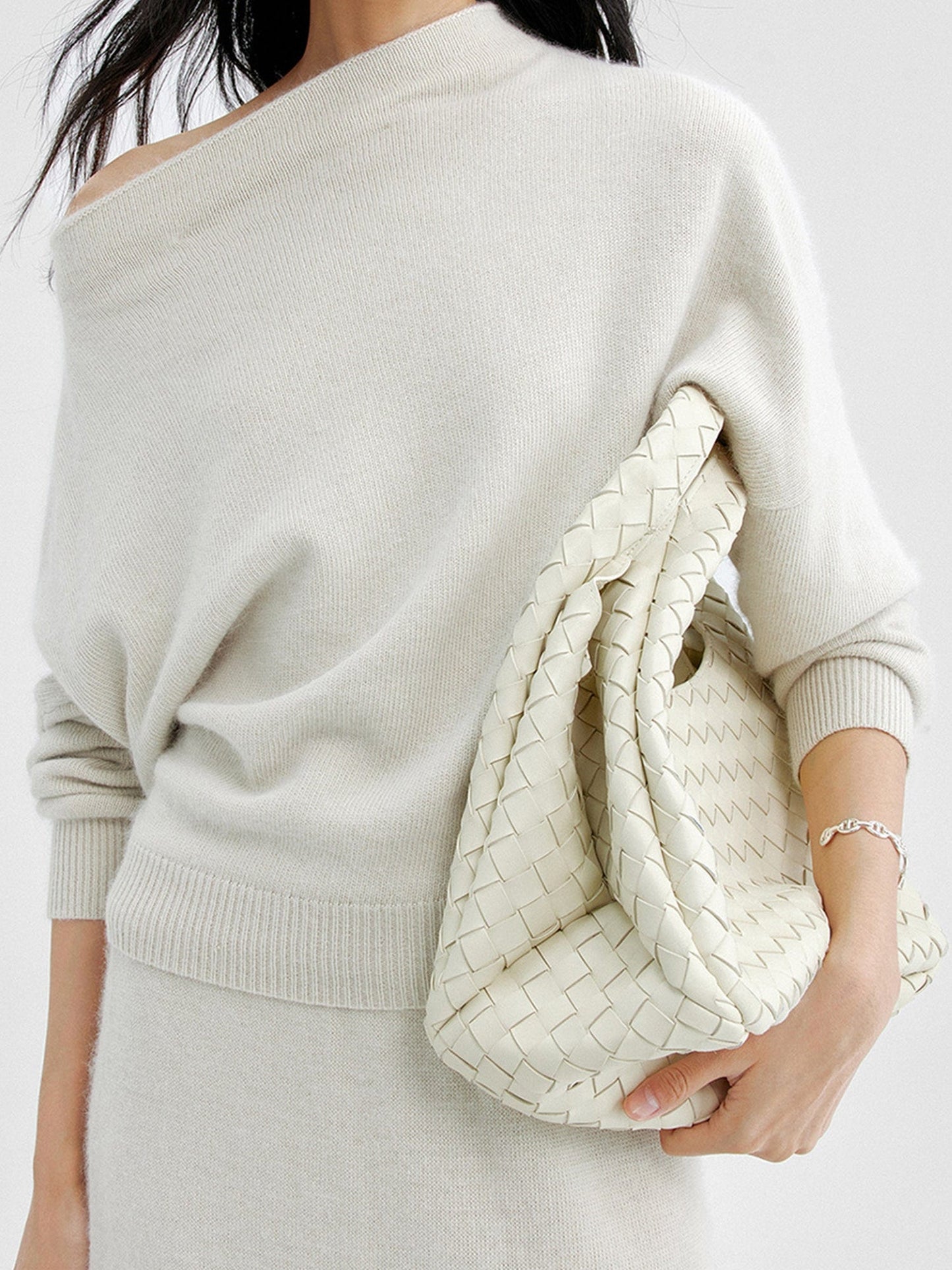 Woman wearing Arkin Studio cold shoulder slim knit top in ivory and matching skirt, holding a white bag, standing facing the camera, on a white background