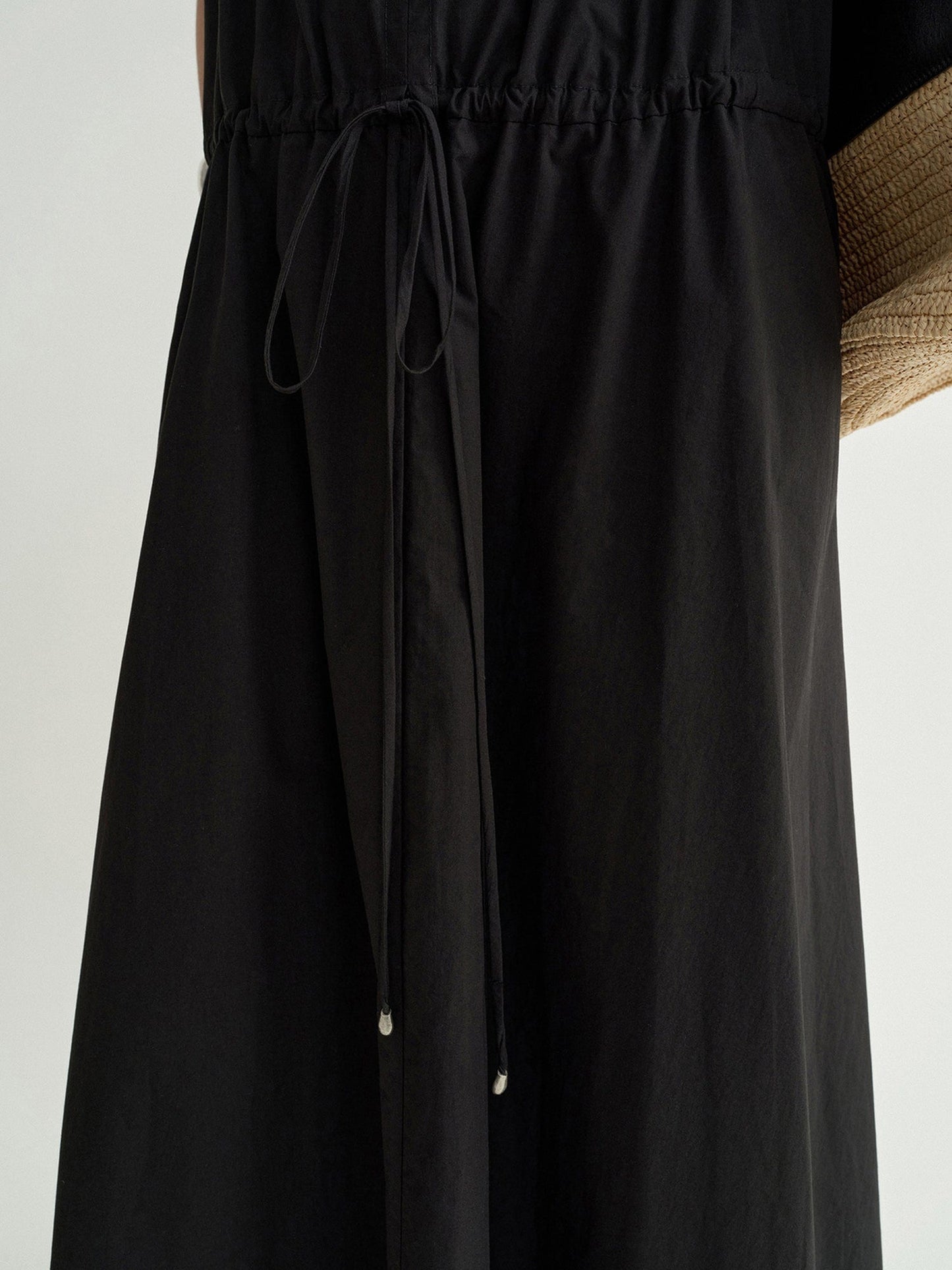 Close-up of a woman's waist wearing Arkin Studio black cotton shift dress with leather collar, standing facing the camera, on a white background"