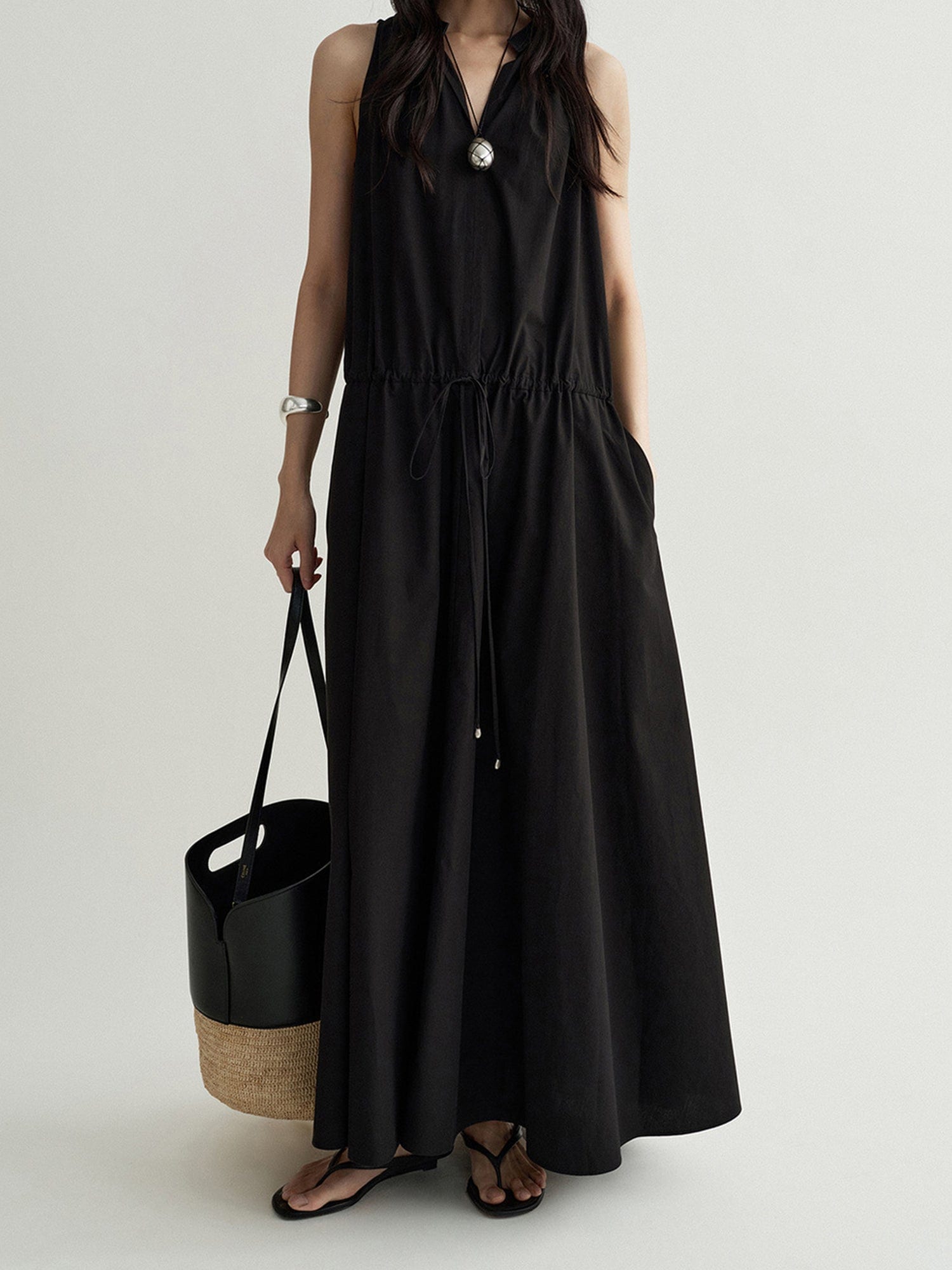 Woman wearing Arkin Studio cotton shift dress with leather collar in black, holding a black bag in right hand, standing facing the camera, on a white background