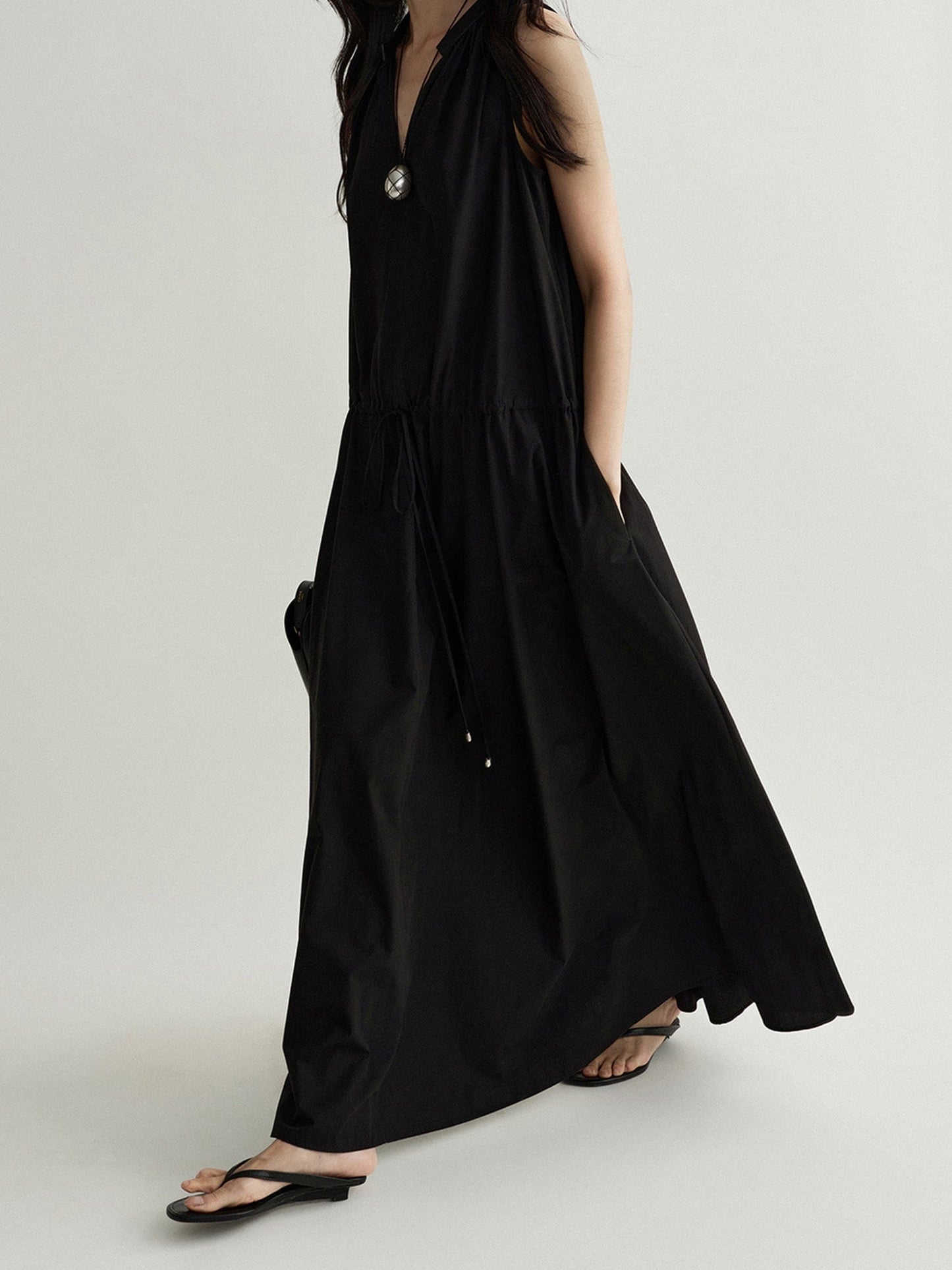 Woman wearing Arkin Studio cotton shift dress with leather collar in black, one hand in the pocket of the dress, walking sideways, on a white background