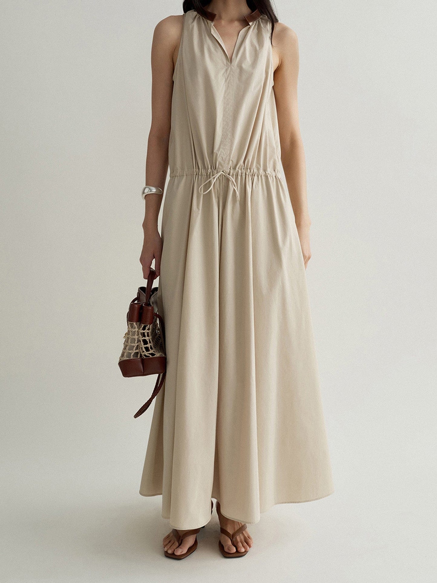 Woman wearing Arkin Studio cotton shift dress with leather collar in cream, holding a brown bag in right hand, standing facing the camera, on a white background