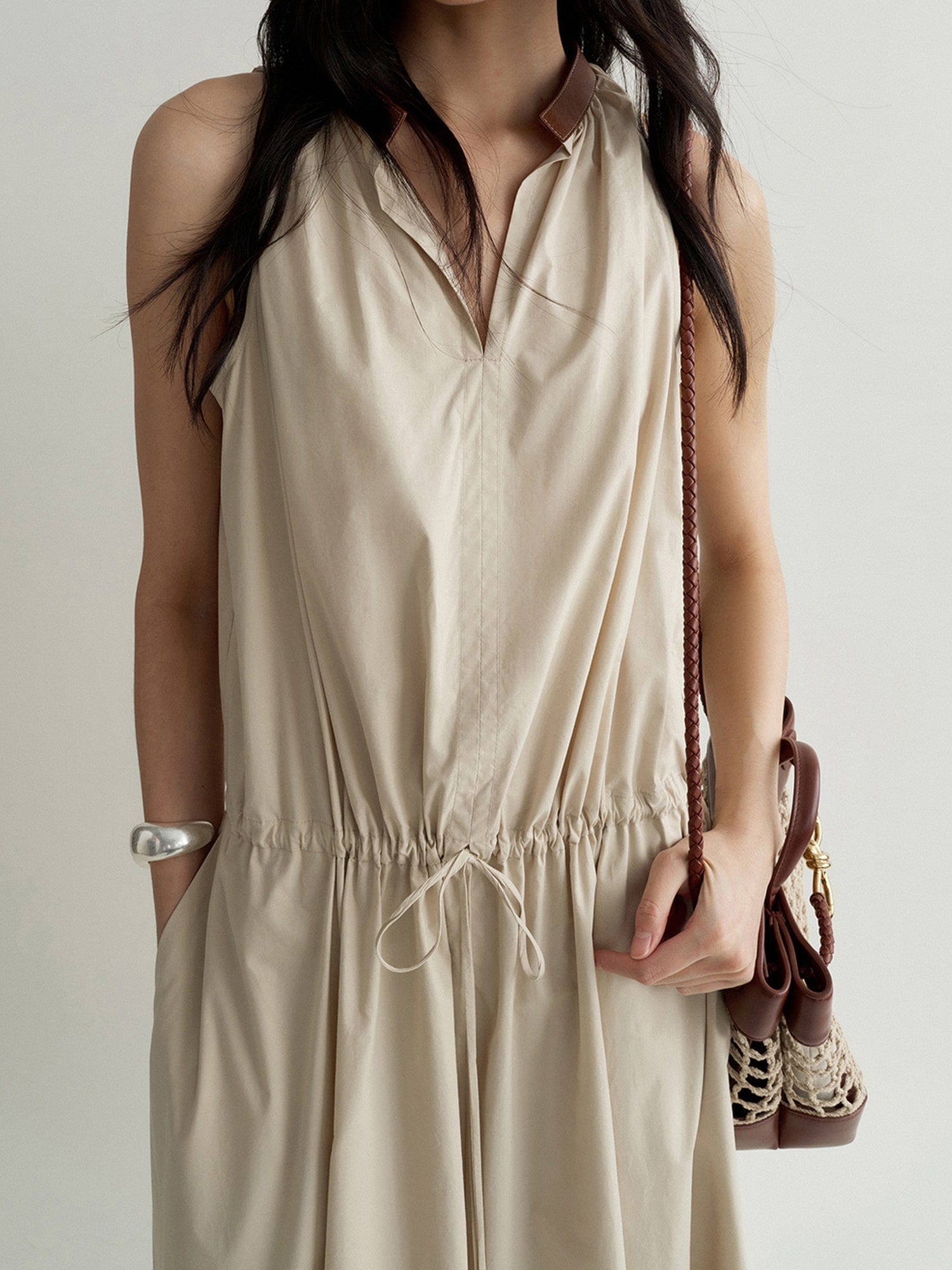 Woman wearing Arkin Studio cotton shift dress with leather collar in cream, with a brown bag on her left shoulder, standing facing the camera, on a white background