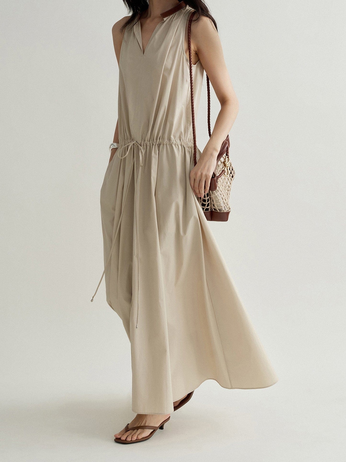 Woman wearing Arkin Studio cotton shift dress with leather collar in cream, with a brown bag on her left shoulder, walking sideways, on a white background