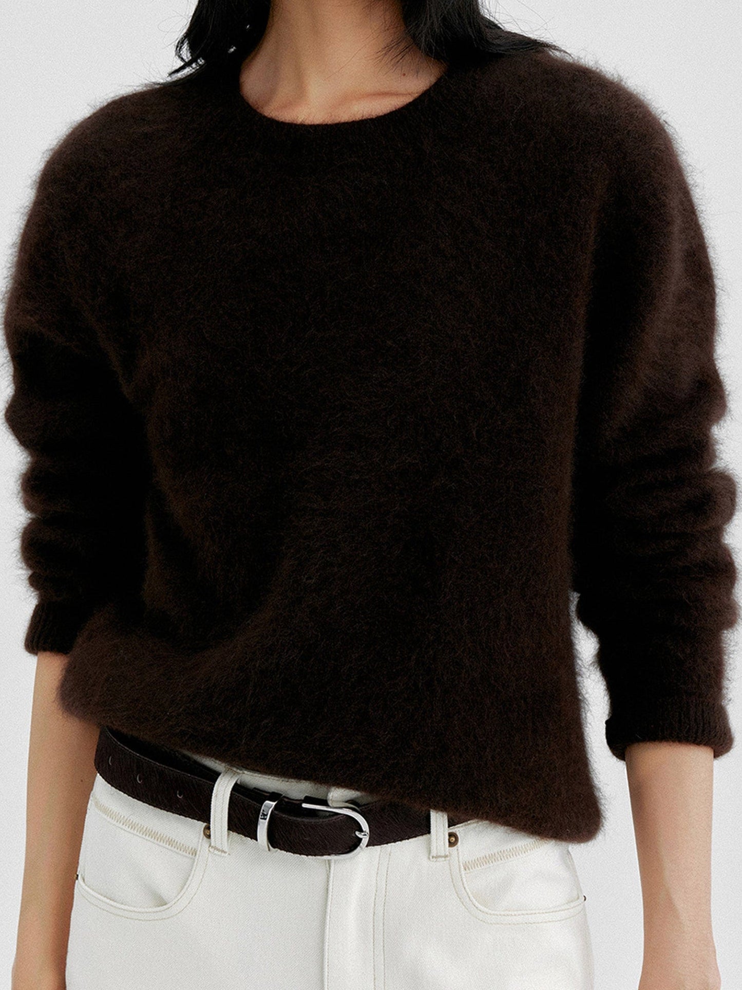 Woman wearing Arkin Studio cozy crewneck wool sweater in dark-brown and matching white pants with a dark brown belt, hands down at her sides, standing facing the camera, on a white background