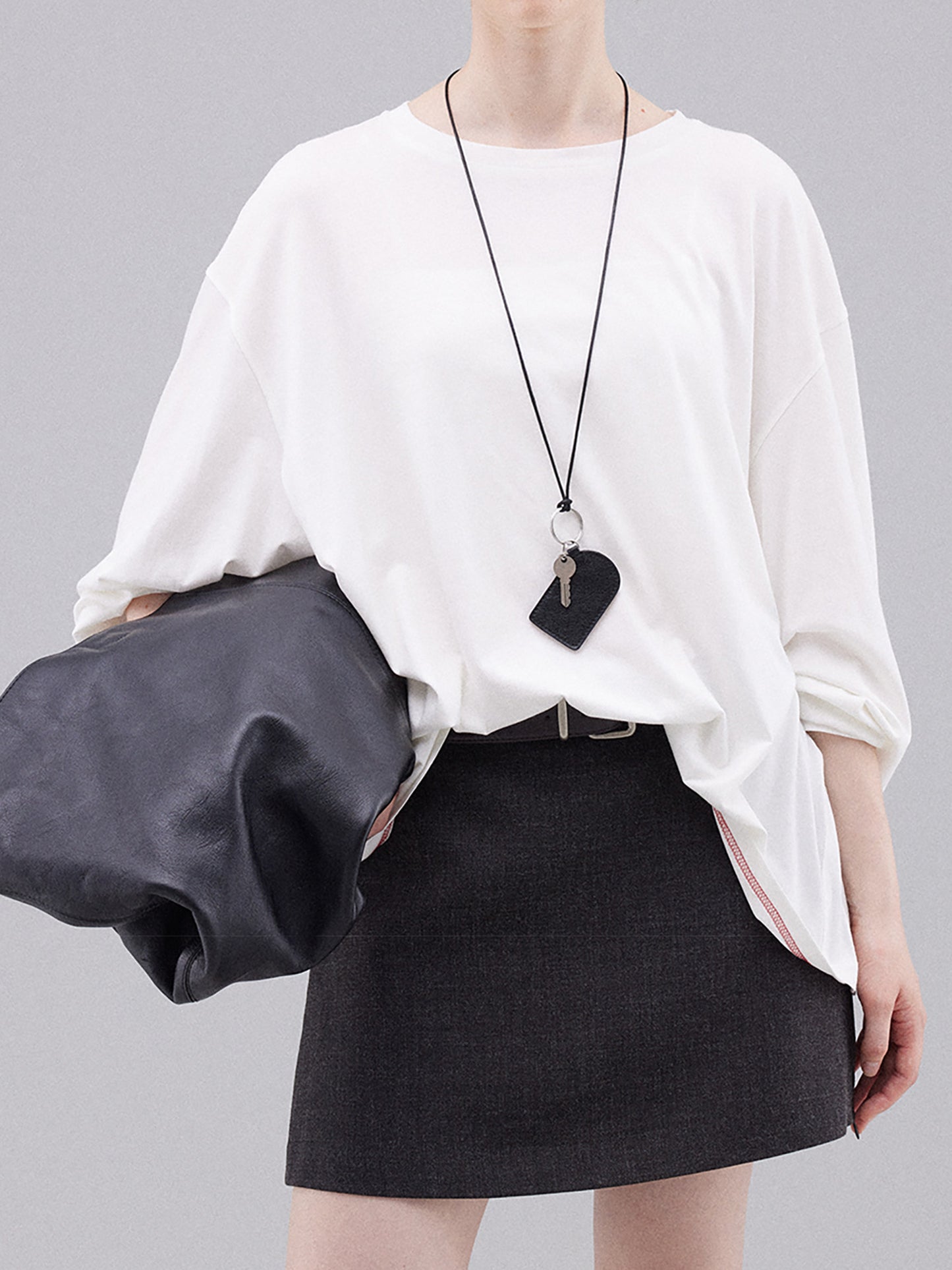 Woman wearing Arkin Studio deconstructed modal cotton long sleeve tee in white and a black skirt, holding a black handbag, standing facing the camera, on a white background