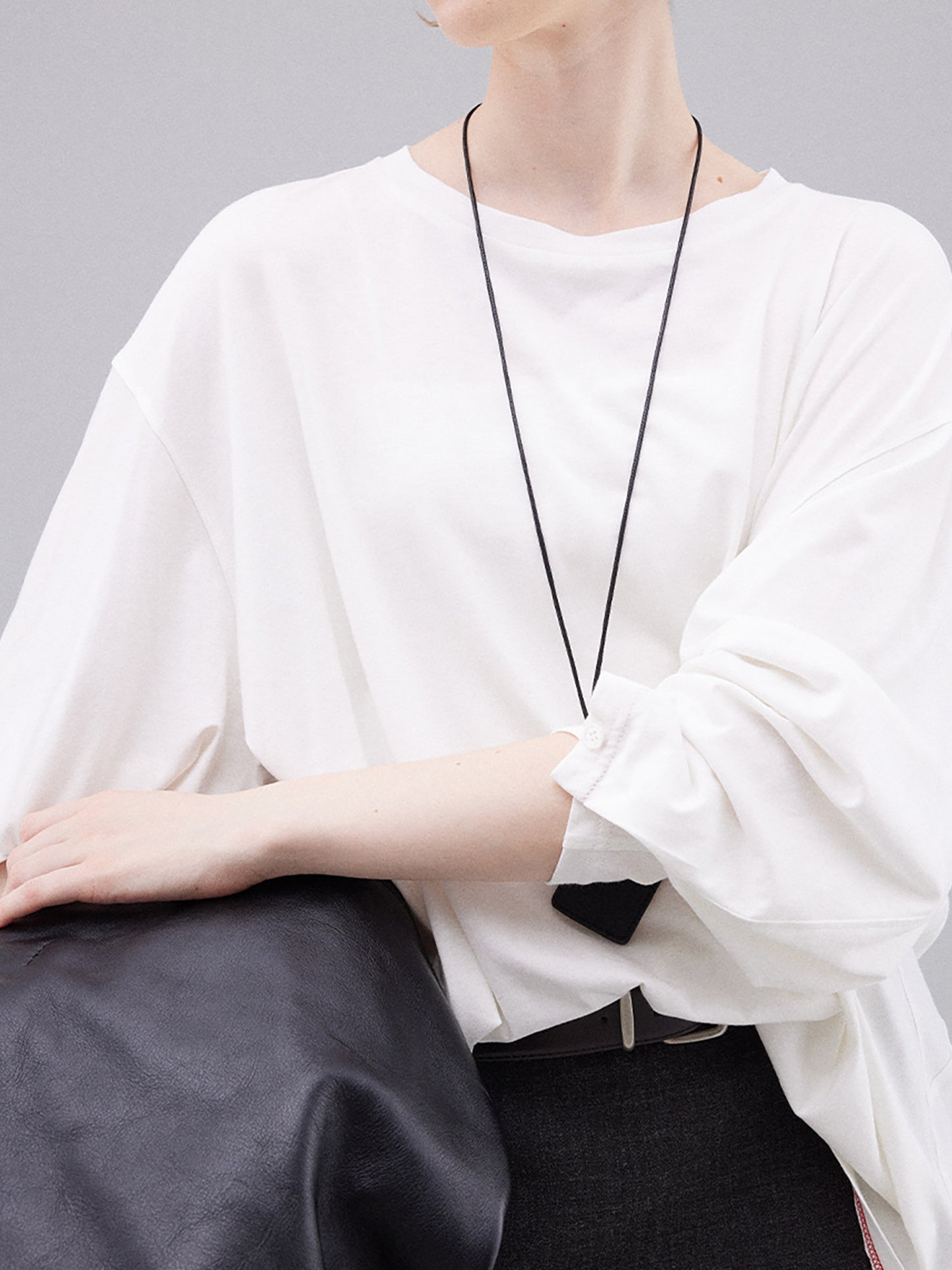 Woman wearing Arkin Studio deconstructed modal cotton long sleeve tee in white and a black skirt, holding a black handbag, standing facing the camera, on a white background