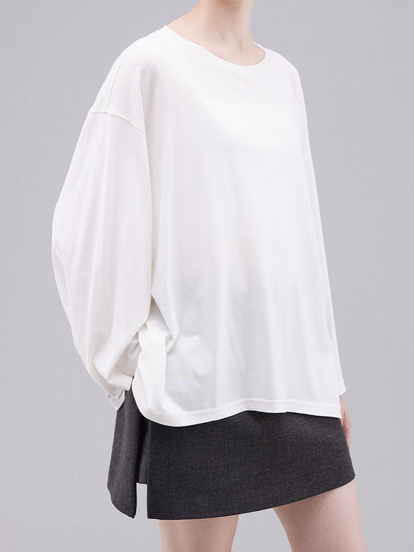 Woman wearing Arkin Studio deconstructed modal cotton long sleeve tee in white and a black skirt, standing sideways, facing the camera, on a white background