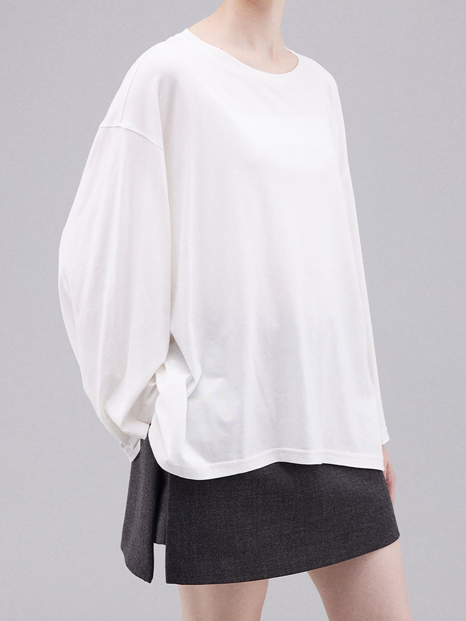 Woman wearing Arkin Studio deconstructed modal cotton long sleeve tee in white and a black skirt, standing sideways, facing the camera, on a white background