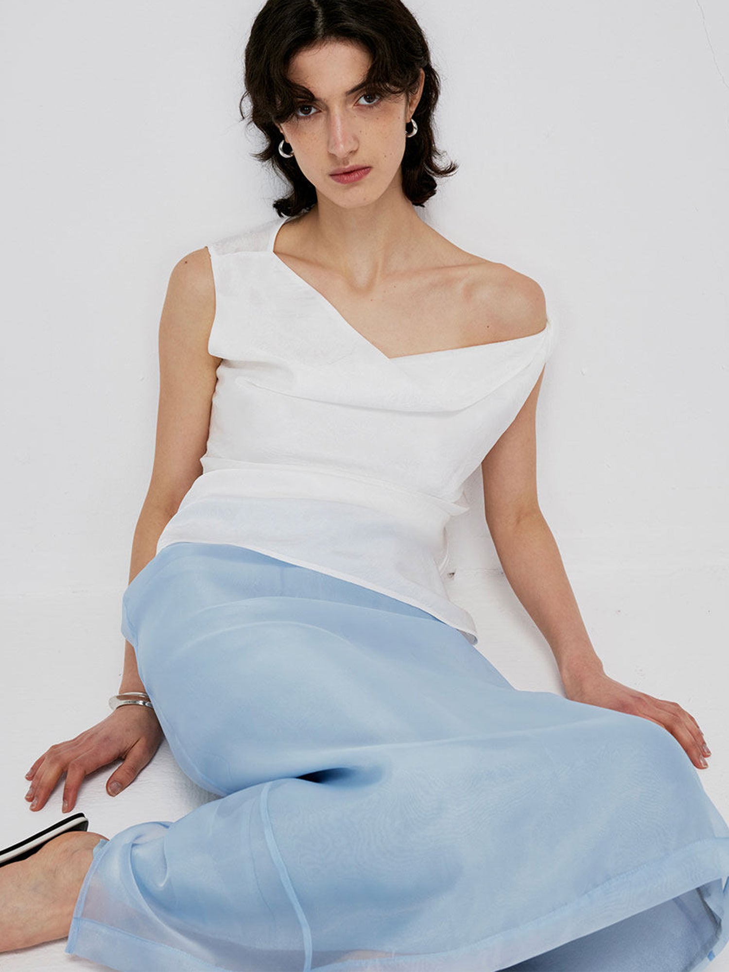 Woman wearing Arkin Studio high-waist mesh two-layer midi skirt in light blue, sitting and facing the camera, on a clean light gray background