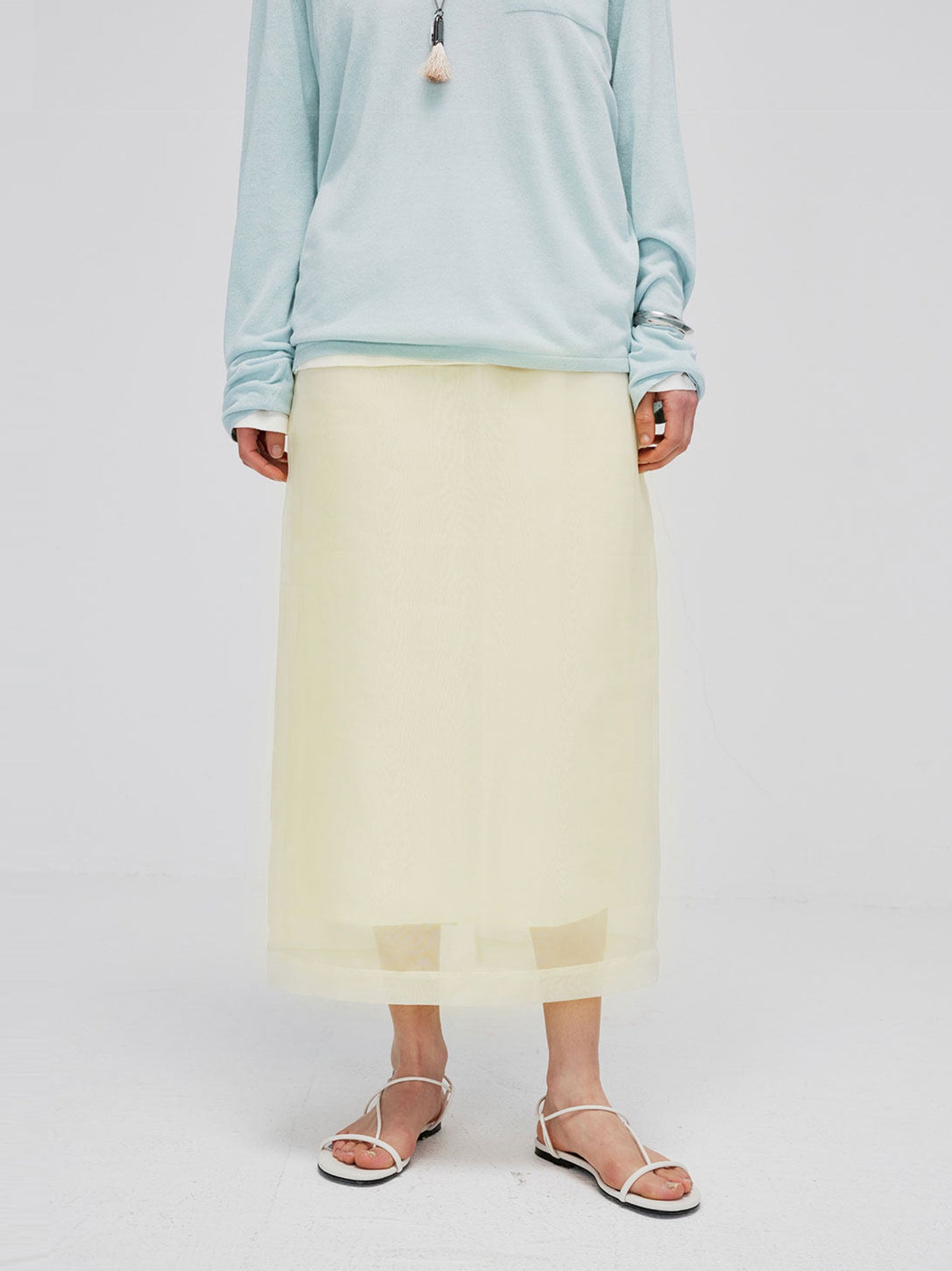 Woman wearing Arkin Studio high-waist mesh two-layer midi skirt in light yellow and a light blue long sleeve, standing facing camera, on white background
