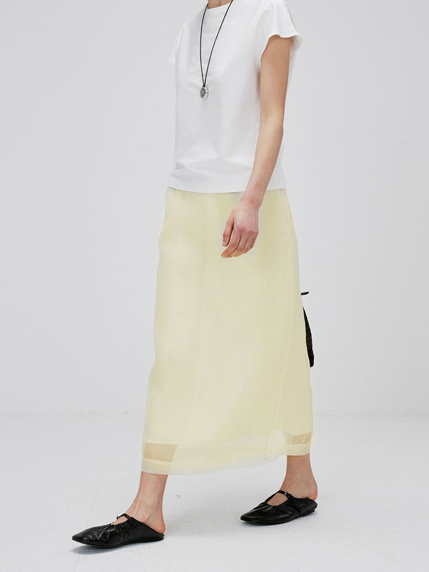 Woman wearing Arkin Studio high-waist mesh two-layer midi skirt in light yellow and a white short sleeve, walking on white background