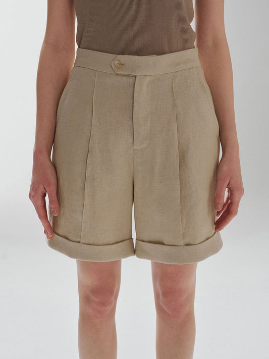 Woman wearing Arkin Studio high waist turn up linen shorts in khaki and a brown top, standing with arms down at her sides, facing the camera, on a white background