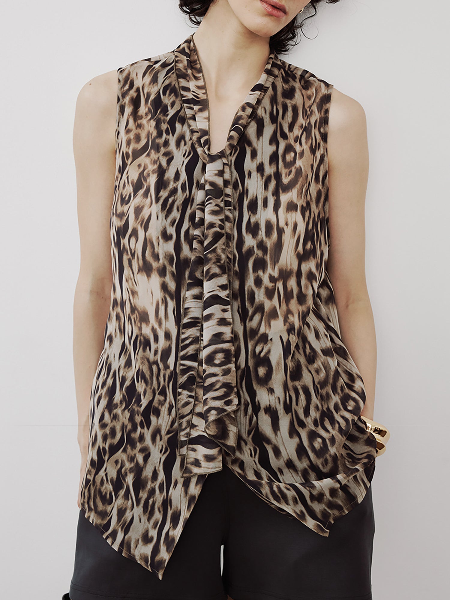 Woman wearing Arkin Studio leopard chiffon v-neck tie blouse in brown and black shorts, standing facing the camera, on a white background