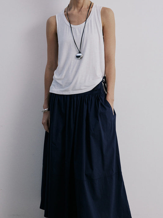 Woman wearing Arkin Studio lightweight pleated a-line drawstring skirt in dark-navy and a white sleeveless top, facing the camera, on a white background