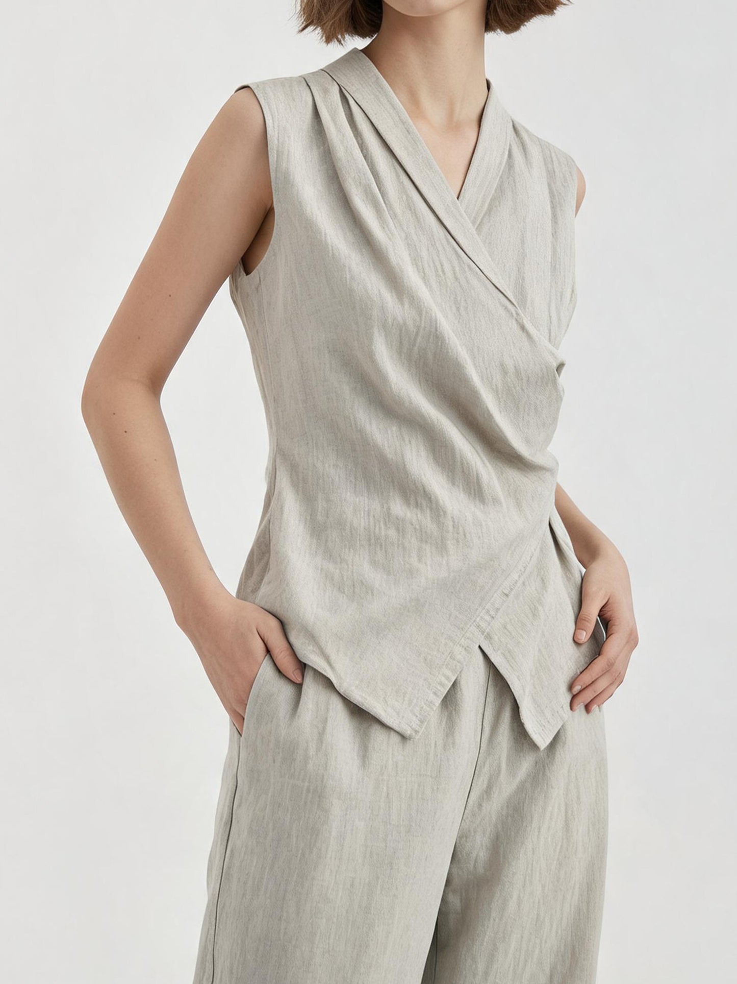 Woman wearing Arkin Studio linen v-neck d-ring vest in light-gray and matching trousers, one hand in the trousers, standing facing the camera, on a white background