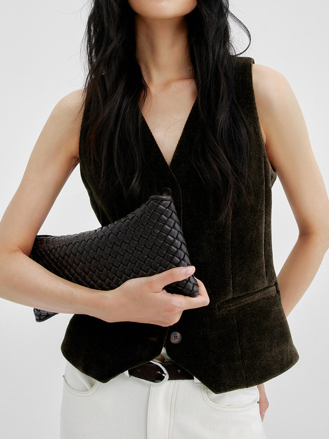 Lookbook: Woman wearing Arkin Studio corduroy v-neck vest in dark olive and matching trousers in white, holding a black handbag, standing facing the camera, on a white background - shop the lookbook