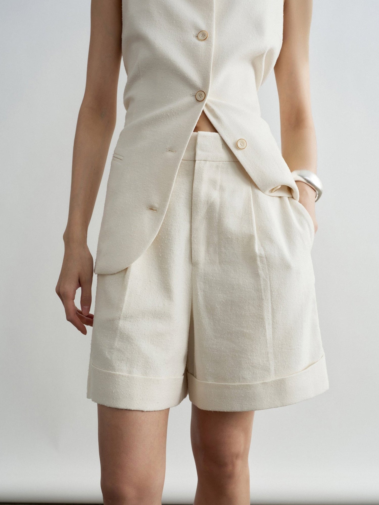 Woman wearing Arkin Studio minimalist cuffed a-line shorts in ivory and matching sleeveless top, standing facing the camera, on a white background