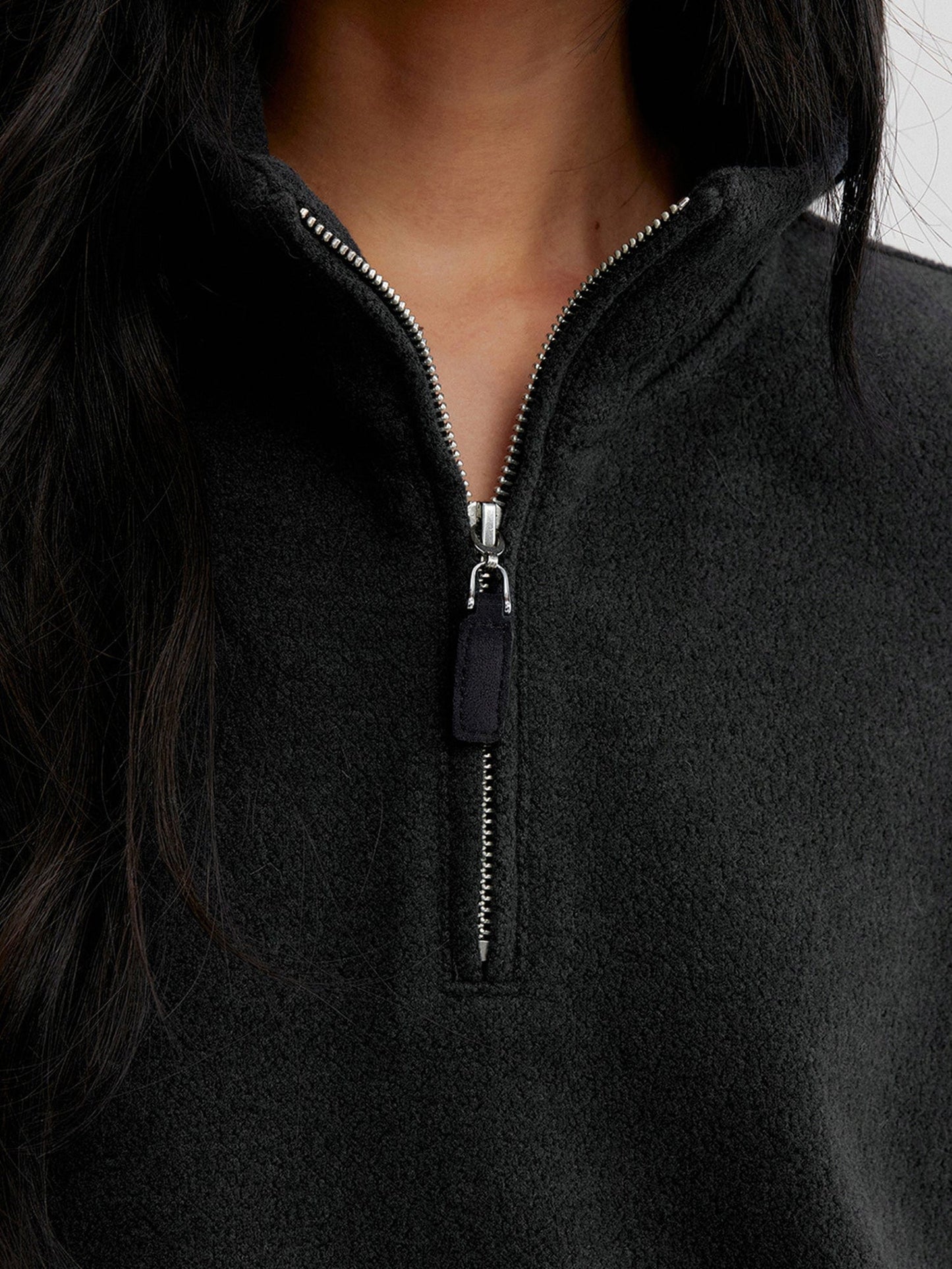 Close up of a woman wearing Arkin Studio minimalist half zip sweatshirt in charcoal, focus on her neck to chest, standing facing the camera, on a white background