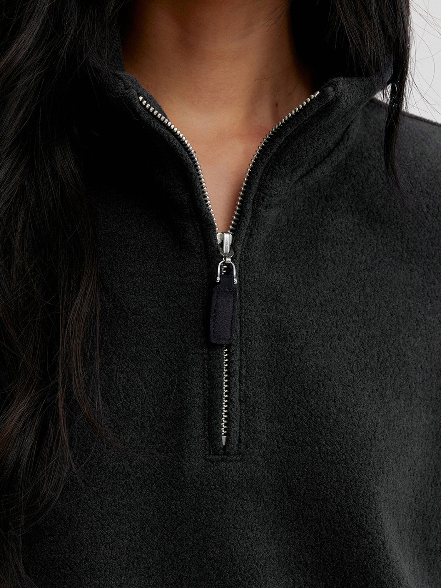 Close up of a woman wearing Arkin Studio minimalist half zip sweatshirt in charcoal, focus on her neck to chest, standing facing the camera, on a white background