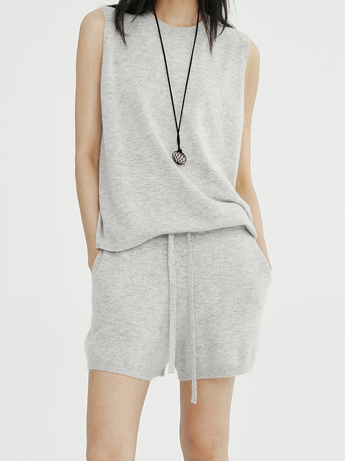 Woman wearing Arkin Studio minimalist round neck tank top in light-gray and matching shorts, hands in pockets, standing facing the camera, on a white background