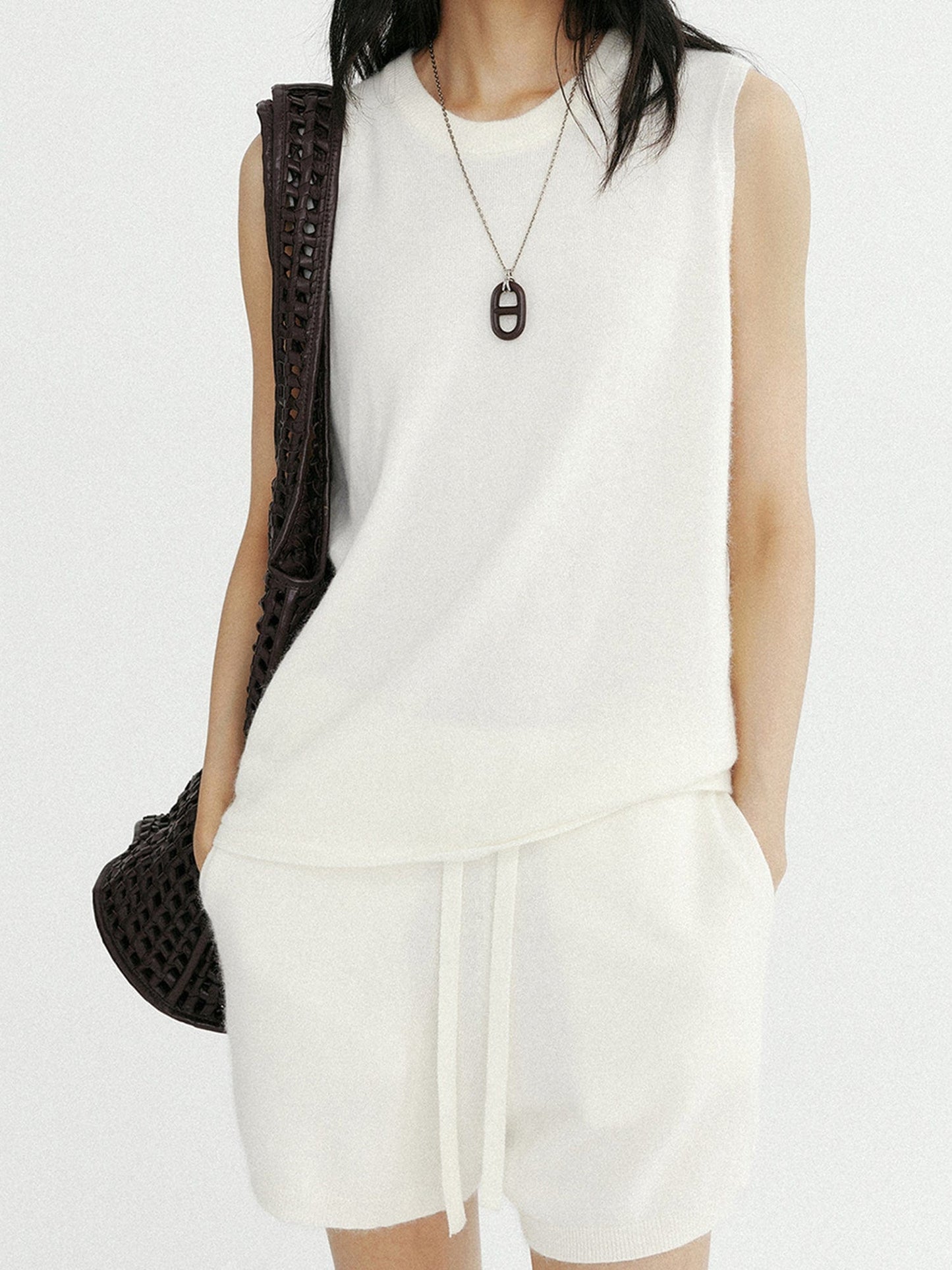 Woman wearing Arkin Studio minimalist round neck tank top in white and matching shorts with a brown bag on her right shoulder, hands in pockets, standing facing the camera, on a white background