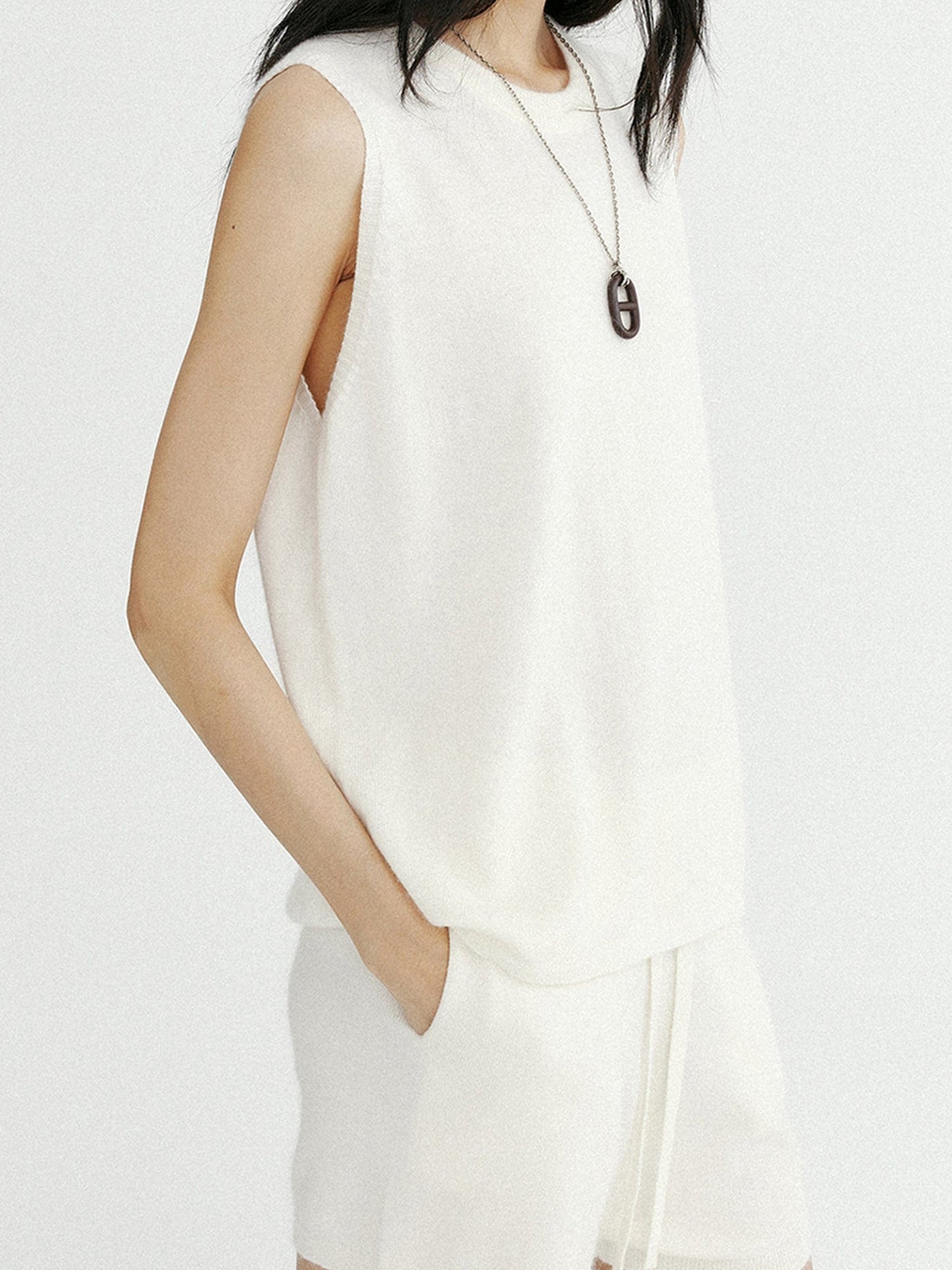 Woman wearing Arkin Studio minimalist round neck tank top in white and matching shorts, hands in pockets, standing sideways, on a white background