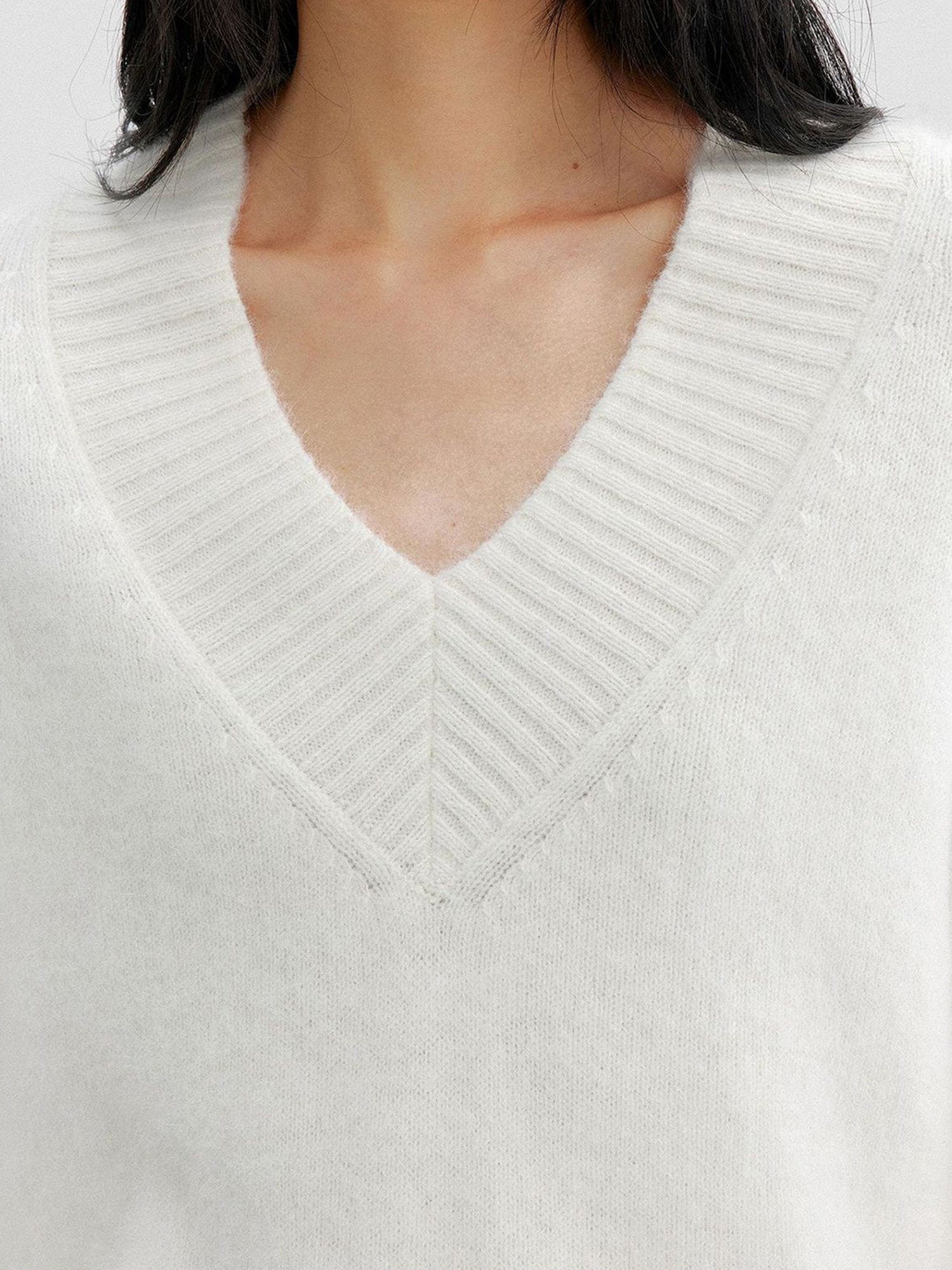 Close-up of the v-neck area of a woman wearing Arkin Studio oversized v-neck fuzzy sweater in white, facing the camera, on a white background