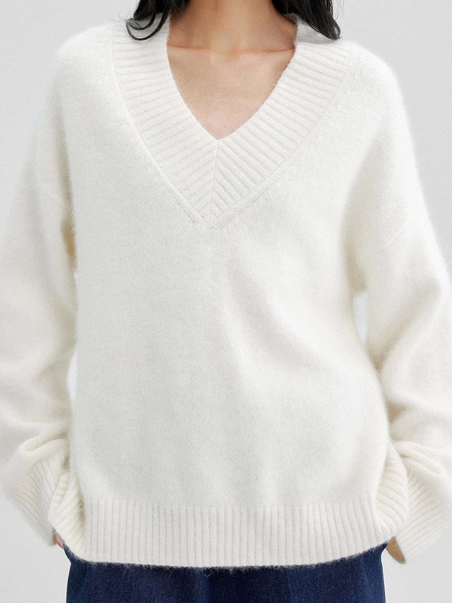 Woman wearing Arkin Studio oversized v-neck fuzzy sweater in white and matching navy pants, hands in pockets, standing facing the camera, on a white background