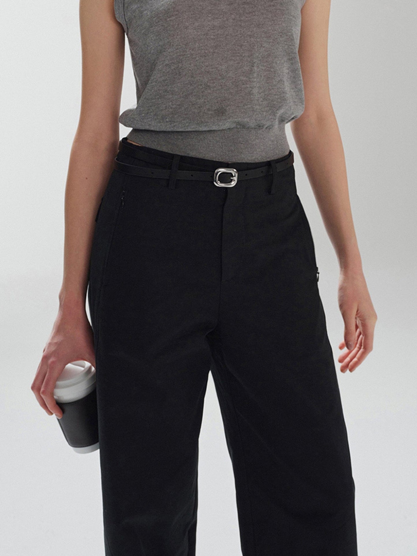 Woman wearing Arkin Studio pear friendly curved leg pants in black and a gray top, with coffee in right hand, standing facing the camera, on a white background