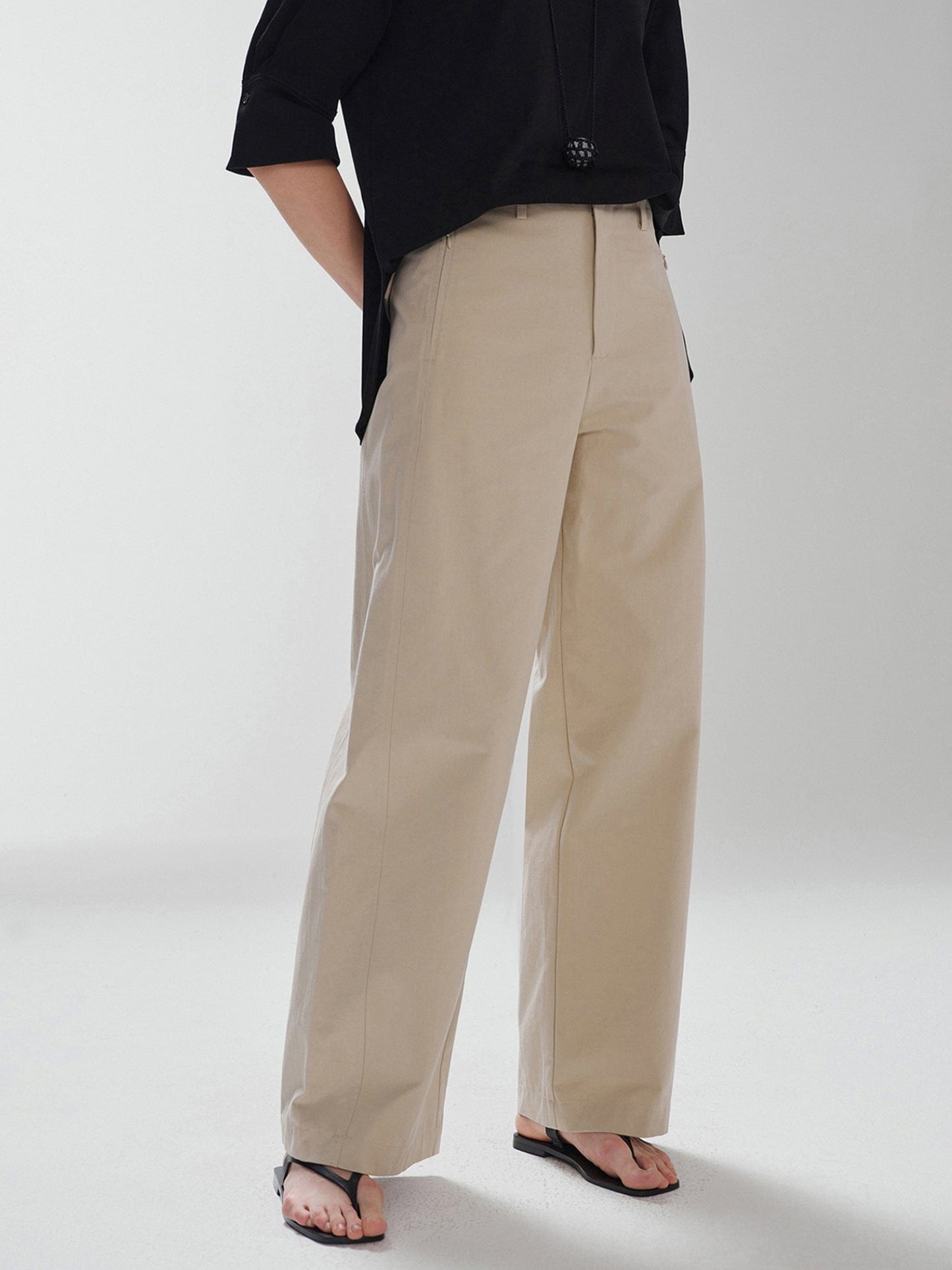 Woman wearing Arkin Studio pear friendly curved leg pants in khaki and a black top, with hands clasped behind her back, body slightly turned to the left, standing facing the camera, main view on a white background