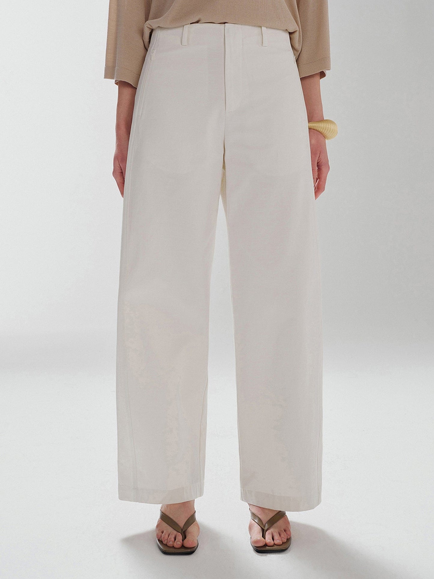 Woman wearing Arkin Studio pear friendly curved leg pants in ivory and a brown top, with arms down at her sides, standing facing the camera, main view on a white background