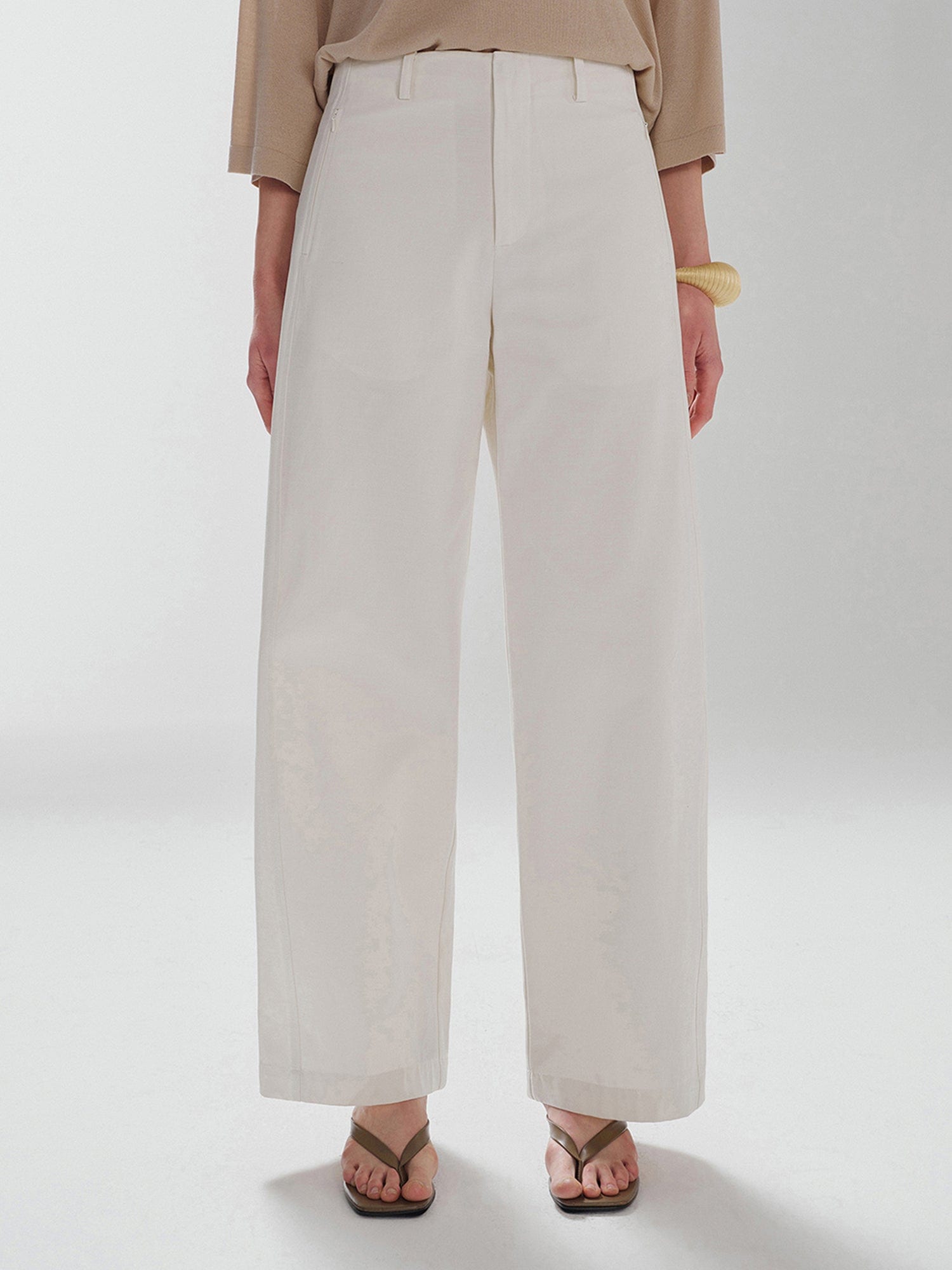 Woman wearing Arkin Studio pear friendly curved leg pants in ivory and a brown top, with arms down at her sides, standing facing the camera, main view on a white background