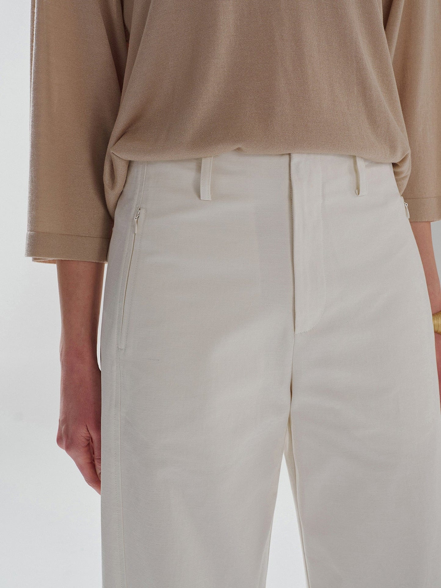 Woman wearing Arkin Studio pear friendly curved leg pants in ivory and a brown top, with arms down at her sides, standing facing the camera, on a white background