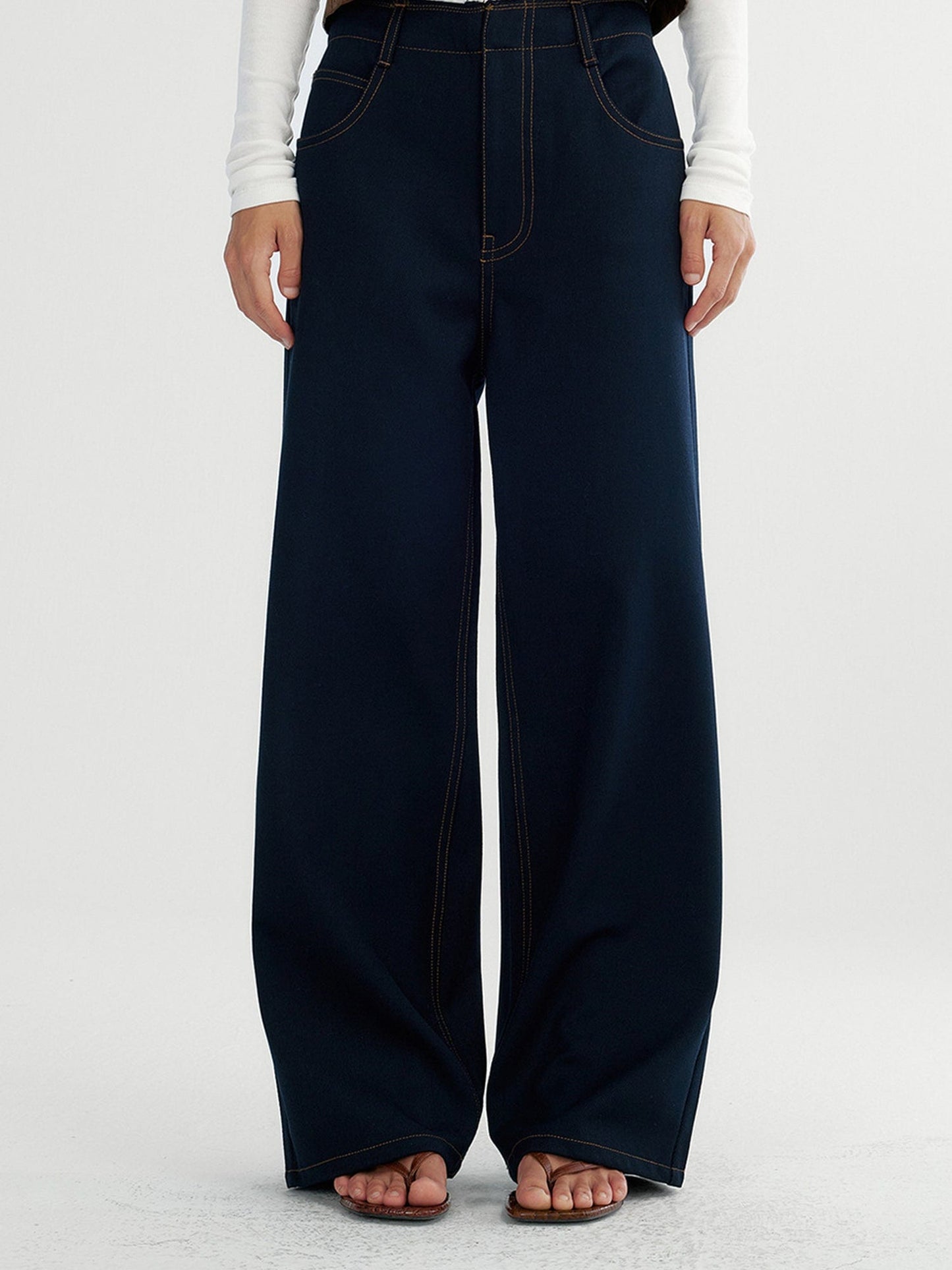 Woman wearing Arkin Studio raw edge contrast stitch trousers in dark navy, with hands down at her sides, standing facing the camera, on a white background